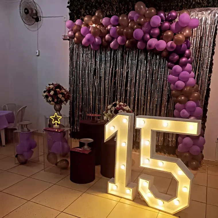 Numeros 15 iluminados na frente de uma cortina de baloes bordo e dourados