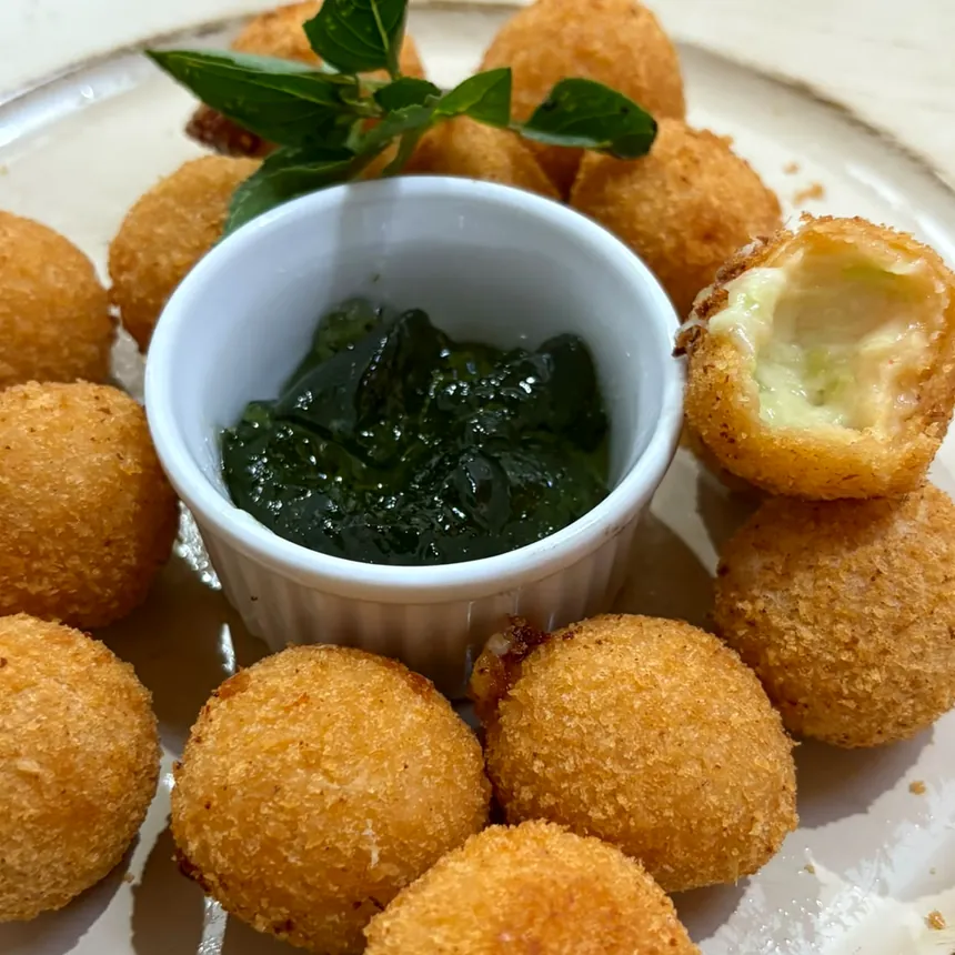 Bolinhos de queijo dourados, um deles partido mostrando o recheio, ao lado da geleia de pimenta
