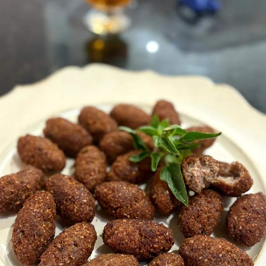 Mini kibes dourados em prato branco, um deles partido mostrando o recheio